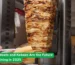 Large vertical stack of grilled meat being sliced for a kebab sandwich at a street-style rotisserie shop with fresh bread